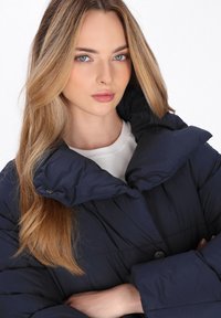 Giacca puffer blu navy con colletto alto, caratterizzata da un design trapuntato e chiusura con bottoni in evidenza. Tessuto morbido e leggero.