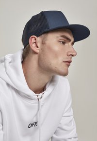 Casquette navy avec un devant solide et un dos en mesh, dotée d'une visière plate. Portée avec un sweat à capuche blanc avec "OFF." brodé en noir.