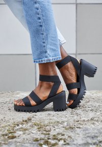 Svarta plattformssandaler med breda tygremmar, öppen tå och en tjock, texturerad klack. Avslappnad stil med en kraftig sula och mjuk finish.