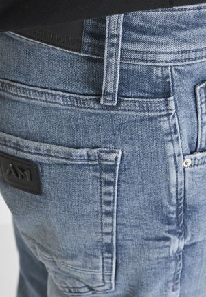 Close-up of blue denim jeans back with visible belt loop, pocket stitching, and two black brand labels reading Antony Morato and AM1.