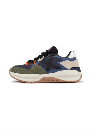 Zapatillas que presentan una mezcla de materiales en azul marino, verde oliva, negro y beige, con una suela acolchada y acentos texturizados. Los cordones son negros.