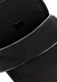 Černý vnitřek tašky s velkou kapsou na zip a menším oddílem na zip se stříbrnými kovovými zipy.