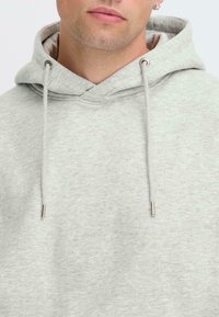Jasnoszara bluza z kapturem wykonana z miękkiego materiału, z dekoltem w kształcie litery V, dwoma sznurkami z metalowymi końcówkami i podszytą wnętrzem.