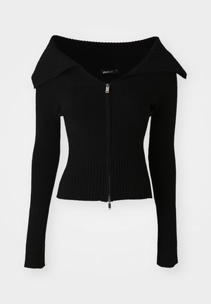 Cárdigan negro acanalado con un gran cuello, mangas largas y cierre frontal con cremallera. La tela parece suave y texturizada.