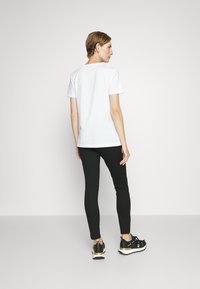 Hvit kortermet T-skjorte med rund hals er kombinert med svarte slim-fit leggings og svarte joggesko med gullakenter.
