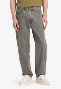 Vaqueros de mezclilla gris de corte holgado, con cinco bolsillos y cierre de botón en la parte delantera. Combinados con zapatillas blancas. Textura suave con un acabado desgastado.