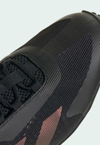 Zwarte sportschoen met een gestructureerde bovenkant, voorzien van mesh panelen, een gladde rubberen neuskap en subtiele metallic accenten aan de zijkant.