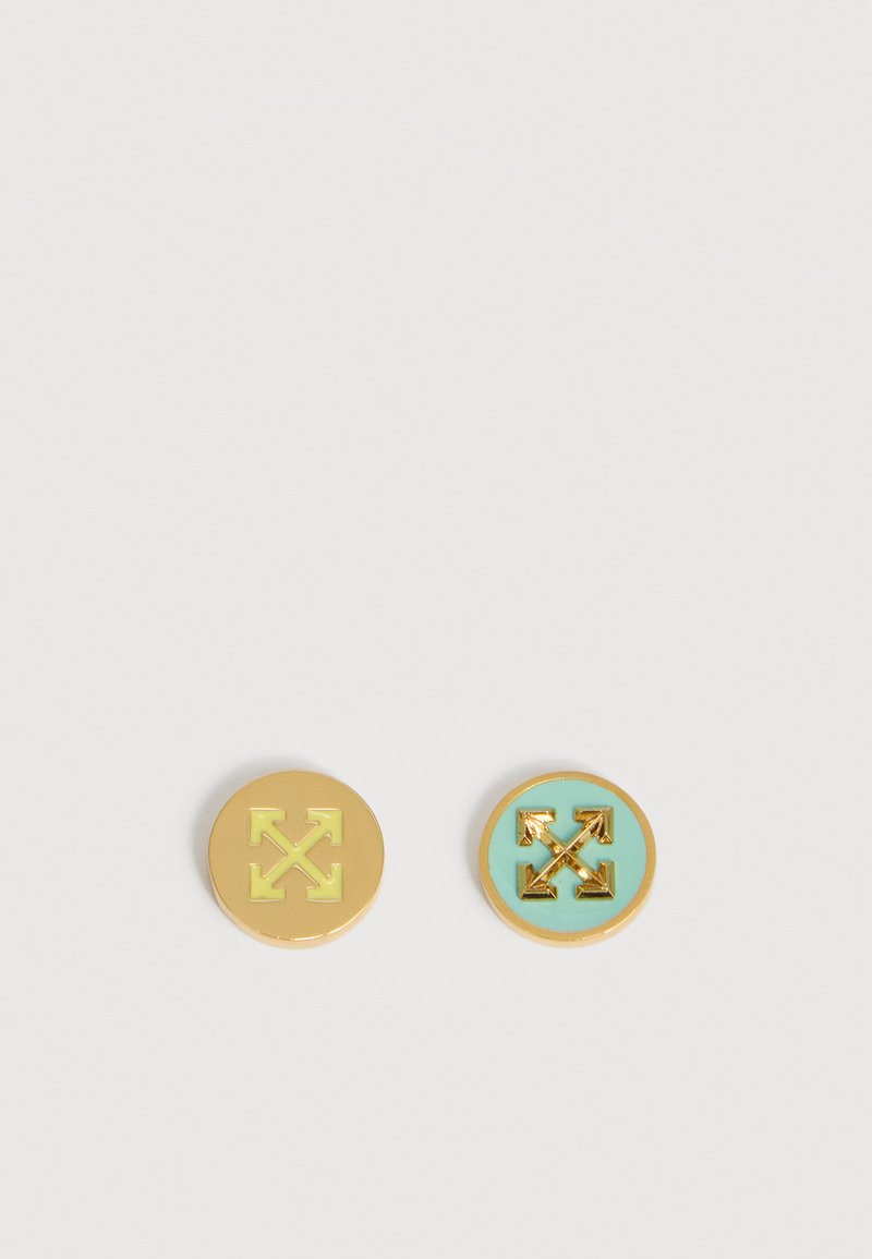 Δύο στρογγυλά μεταλλικά καρφίτσα με χρυσά εικονίδια βελών· το ένα έχει κίτρινο φόντο, το άλλο τιρκουάζ φόντο.