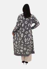 Cardigan lungo grigio con un motivo astratto bianco, polsini e orlo a costine, con tasche laterali e apertura frontale.