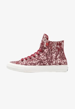 Zapatilla deportiva de caña alta con patrón pixelado rojo y blanco, cordones rojos, ojales metálicos y suela de goma blanca.