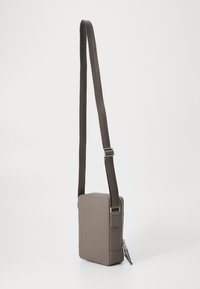 Fyrkantig tvärsöverväska i strukturerat grått material med dragkedjestängning och justerbar rem. Har en stilig, minimal design.