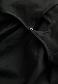 Tessuto nero con una texture liscia, caratterizzato da una chiusura a bottone nella parte superiore. Il design ha uno stile semplice e funzionale.