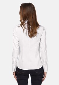 Chemise blanche à manches longues avec une coupe ajustée, ourlet droit et poignets à boutons ; texture lisse avec de subtils détails de couture.