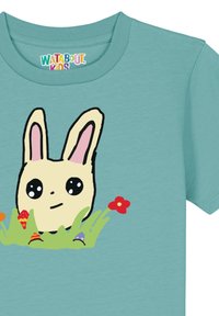 Hellblaue Baumwoll-T-Shirt mit einem Cartoon-Hasen mit großen Augen, rosa Ohren, der im grünen Gras sitzt, umgeben von bunten Blumen und dekorativen Gegenständen.