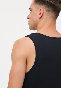 Sort ribbet tanktop med brede stropper, fremvist med et tekstureret stof og en tætsiddende design, vist fra siden og bagfra.