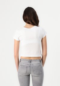 Camiseta blanca corta con mangas cortas, cuello redondo, textura suave, combinada con jeans ajustados grises que cuentan con bolsillos traseros y una cintura de altura media.