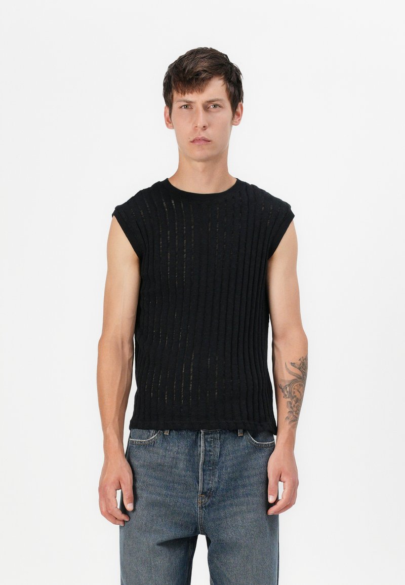 Sort ærmeløs skjorte med ribbet tekstur og vandrette striber, parret med blå denimjeans. Skjorten har en rund udskæring.
