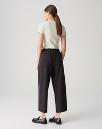 Black wide-leg trousers with an elastic waistband and two back pockets, paired with a light-colored fitted short-sleeve top and black loafers.
