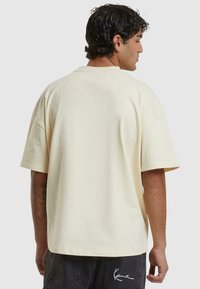 T-shirt oversize de couleur crème, à manches courtes, texture unie, col rond, vue de dos avec des détails de couture subtils. Assorti à un short foncé.