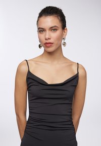 Abito nero con collo a cowl, spalline sottili, design aderente, texture arricciata in vita, abbinato a orecchini metallici a forma di cuore.