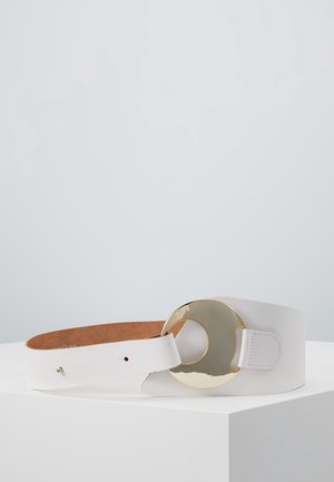 Biały skórzany pasek z szerokim paskiem i dużą, okrągłą, złotą metalową klamrą, prezentowany zwinięty na białej powierzchni na jednolitym tle.