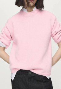 Pink knit sweater with a round neckline, dropped shoulders, ribbed cuffs and hem. The fabric appears soft, worn over a white collared shirt.