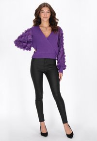 Suéter morado tipo envolvente con mangas abullonadas texturizadas, combinado con pantalones ajustados negros y tacones negros. Material de punto suave, diseño de escote en V profundo.