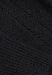 Primo piano di un tessuto nero lavorato a maglia che mostra file diagonali di occhielli e un motivo a coste testurizzato su un tessuto morbido.