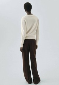 Pull en tricot crème à manches longues, avec un col montant, associé à un pantalon large marron foncé. Texture lisse, design minimaliste, couleurs neutres.