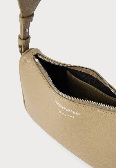 Τσάντα χειρός από μπεζ δέρμα με υφή και φερμουάρ κλεισίματος, με αντίθετη σκουρόχρωμη εσωτερική επένδυση και ανάγλυφο λογότυπο. Περιλαμβάνεται ρυθμιζόμενο λουρί.