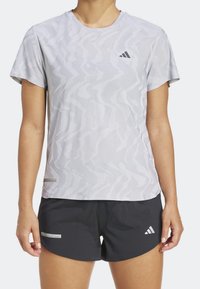 Camiseta deportiva gris con patrón de olas, de mangas cortas y escote redondo, combinada con pantalones cortos negros que presentan una etiqueta sutil.