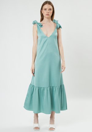 Un vestido sin mangas, de escote en V, en color azul verdoso, con dobladillo con volantes y cintas en los hombros, fabricado en una tela suave con una silueta fluida.