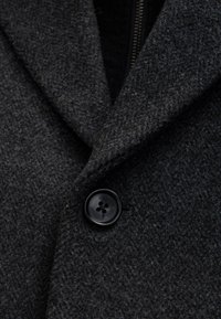 Cappotto di lana grigio carbone con tessuto strutturato, rever appuntiti e dettaglio di bottone nero al colletto.