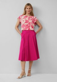 Bloemige blouse met korte mouwen in roze en crème met een gerimpelde halslijn, gecombineerd met een effen roze knie-lange rok. Witte bandjeshakken.