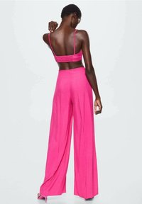 Ensemble en deux pièces rose comprenant un crop top ajusté avec des bretelles réglables et un pantalon à jambes larges, le tout en tissu léger.