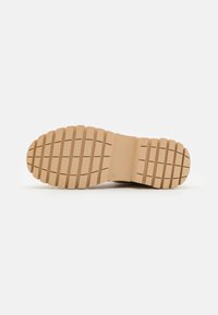 Semelle en caoutchouc beige avec des crampons prononcés et un talon lisse. Présente une forme épurée et streamline adaptée à divers styles de chaussures.