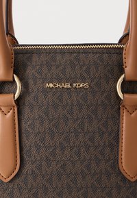 Καφέ τσάντα χειρός με μονόγραμμα και καφέ δερμάτινες λεπτομέρειες. Διαθέτει χρυσά μεταλλικά στοιχεία και φερμουάρ, με υφή επιφάνειας που παρουσιάζει ξεχωριστό μοτίβο.