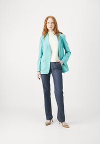 Blazer turchese, dolcevita bianca, pantaloni in denim scuro e tacchi beige. Il blazer è caratterizzato da un solo bottone e due tasche frontali.