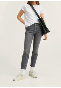 Jeans in denim grigio, t-shirt bianca a maniche corte e sneakers bianche con suole grigio chiaro. Una borsa nera a tracolla poggia sull'anca.