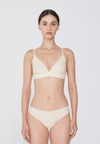 Světlý béžový bralet s výstřihem do V a tenkými ramínky, doplněný o odpovídající bikiny, vyrobený z hladkého materiálu s bezešvým povrchem.