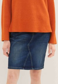 Tmavě modrá džínová sukně s přiléhavým střihem, která má výrazný šev a lem, který končí těsně nad kolenem.