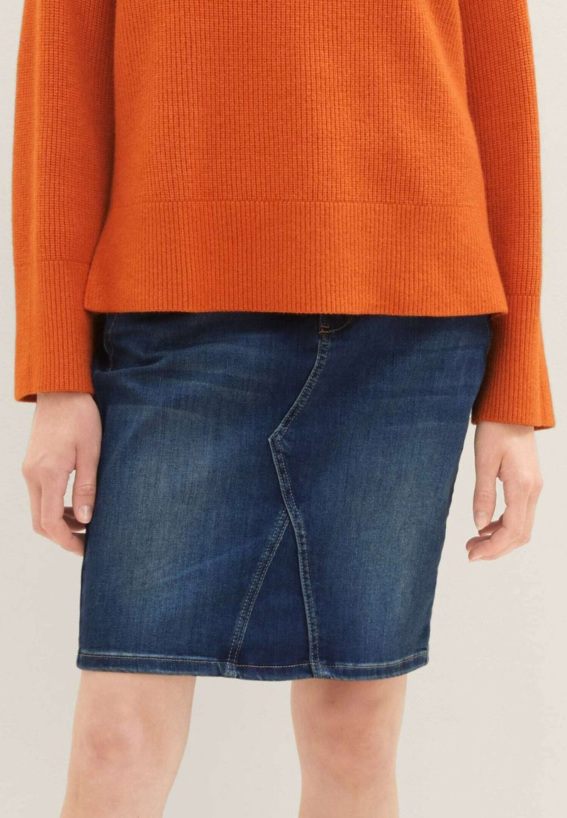 Tmavě modrá džínová sukně s přiléhavým st řihem, která má výrazný šev a lem, který končí těsně nad kolenem.