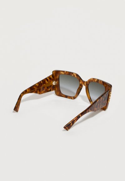 Τετράγωνες γυαλιά ηλίου με πλαίσια μοτίβο χελώνας και φακούς με διαβαθμισμένη γκρι απόχρωση, ακουμπισμένα σε φωτεινή επιφάνεια.