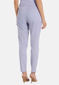 Lila broek met een getailleerd ontwerp, twee achterzakken en een gladde textuur. Gecombineerd met transparante hakken sandalen.