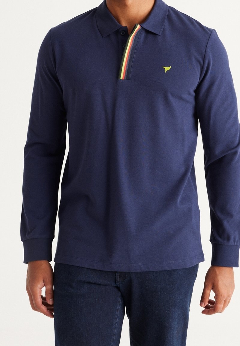 Polo de manga larga en color navy, hecho de algodón, con un cuello a rayas en verde, amarillo y rojo, y un pequeño logo en el pecho.