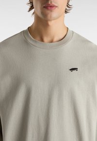 Lichtgrijze katoen sweatshirt met een ronde hals. Heeft een klein zwart skateboardlogo geborduurd aan de linkerkant.