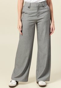 Grijze wijde broek met een textuurafwerking, twee knopen aan de voorkant en zijzakken, gecombineerd met witte sneakers op een neutrale achtergrond.