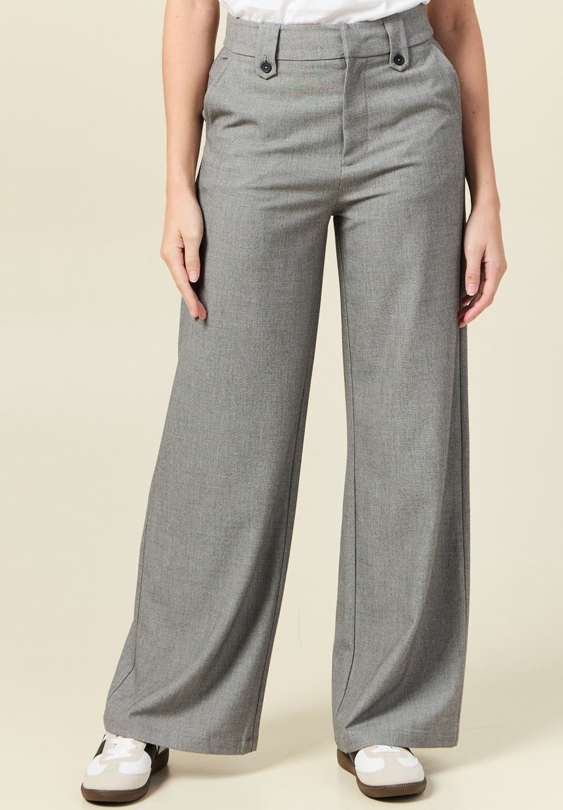 Grijze wijde broek met een textuurafwerking, twee knopen aan de voorkant en zijzakken, gecombineerd met witte sneakers op een neutrale achtergrond.