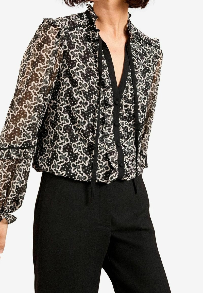 Blusa in bianco e nero con un motivo floreale, tessuto trasparente, colletto arricciato e chiusura con bottoni. Maniche lunghe con polsini elastici.