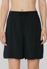 Pantalones cortos negros de tela suave, con una cinturilla elástica y cordón, y dos bolsillos laterales. Textura suave y corte holgado.